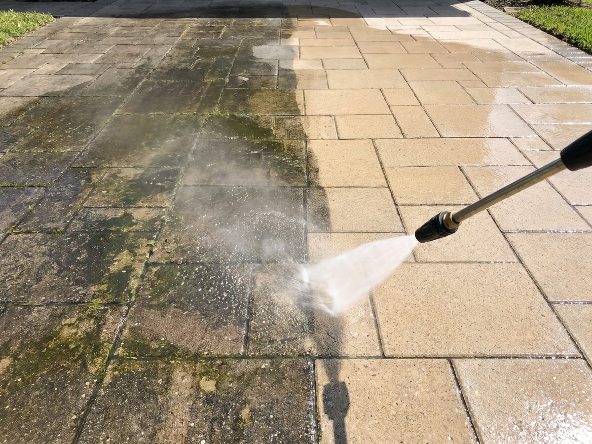 Nettoyage au jet haute pression d’un pavé de béton révélant une surface propre et claire